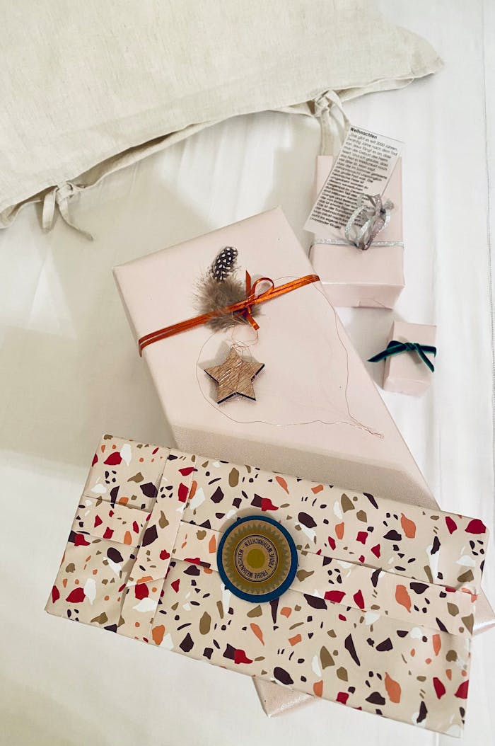 Stylish gift box with star ornament and feather decor on a cozy white bed setting.